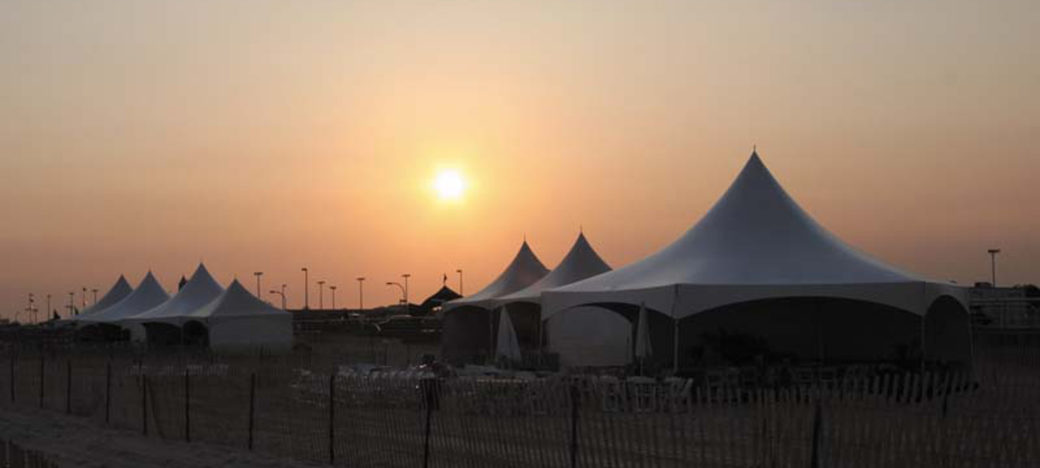 multiple high peak tents setup on a beach at sunset